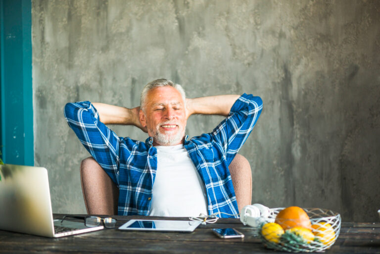 smiling-senior-man-relaxing-chair-with-electronic-device-table